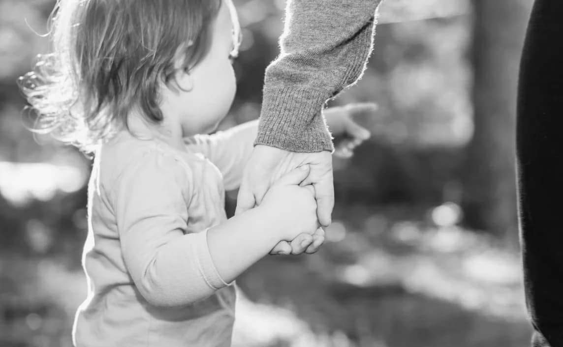 A small child holding tightly to an adult's hand